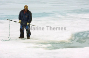 Inuit hunter waiting with harpoon next to seal's breathing hole in sea ice.